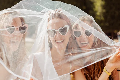 la mariee et ses amies souriantes sous un voile 