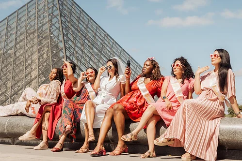 groupe de femmes en robe rose celebrant un evjf a paris devant la pyramide du louvre