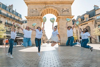 Groupe de femmes sautant devant un arc à Dijon pendant un EVJF, illustrant la joie d’un week-end festif entre amies.