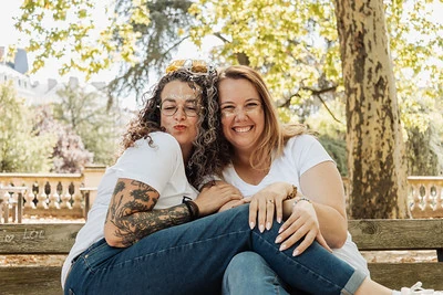 deux femmes complices assises sur un banc en bois dans un parc ensoleillé de Dijon, riant ensemble.