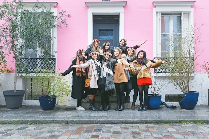 Groupe de femmes posant lors d’un EVJF à Paris devant une façade rose typiquement parisienne, ambiance joyeuse et amicale.