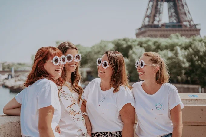 Groupe de femmes souriantes lors d’un EVJF à Paris, posant devant la Tour Eiffel sous un ciel ensoleillé.