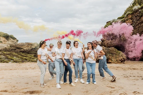 groupe de femmes riant sur la plage avec des fumigènes colorés lors d’un shooting photo evjf à biarritz