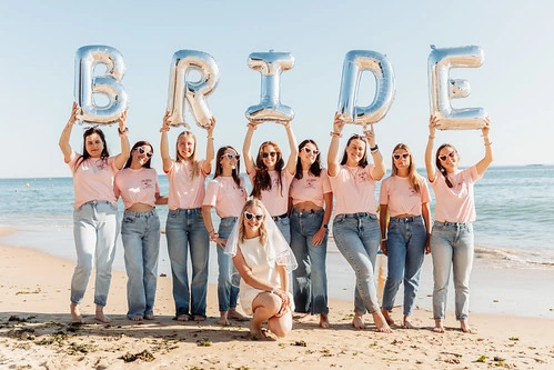 groupe de femmes en jean et t shirt rose tenant des ballons bride sur la plage lors d’un shooting photo evjf à la baule
