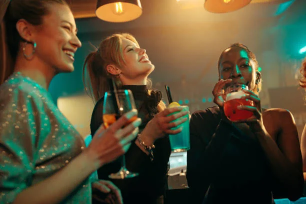 Trois amies rient et trinquent avec des cocktails colorés pendant une soirée 
