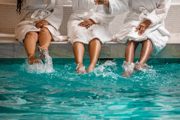trois femmes en peignoir assises au bord d’une piscine d’un spa 