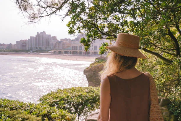 Femme portant un chapeau observant la côte lors d’une visite guidée , avec vue sur la plage et les bâtiments du front de mer.