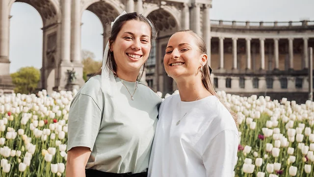 deux femmes souriantes posant devant les arches et les tulipes du parc du cinquantenaire à bruxelles lors d’une visite evjf
