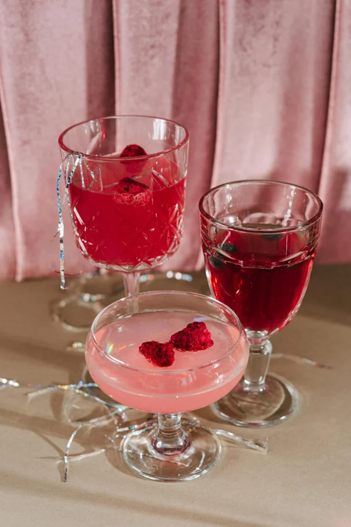 Trois cocktails roses garnis de framboises posés sur une table décorée.